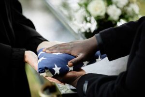 A small group gathered by a graveside with flowers during a daytime outdoor ceremony.