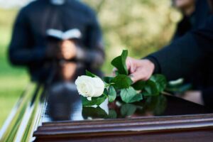 A simple wooden casket surrounded by wildflowers and native grass in a peaceful outdoor setting